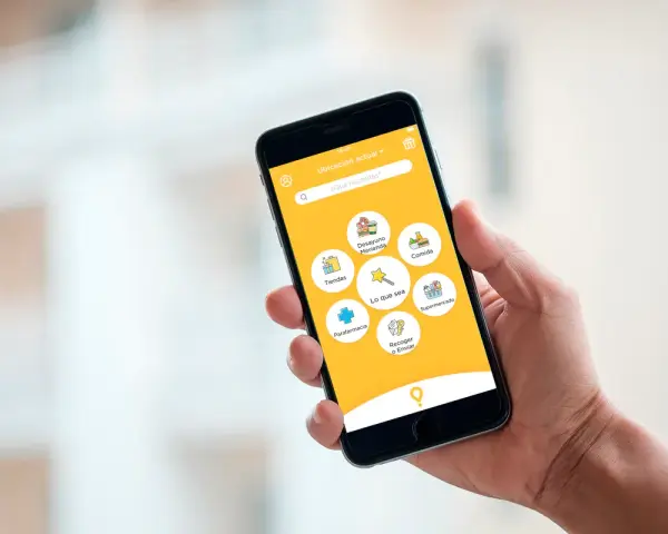 Mano sujetando un smartphone con la app Glovo. Se ven iconos de comida, tiendas, farmacia y supermercado. Interesado en cuanto cobra Glovo a los restaurantes.