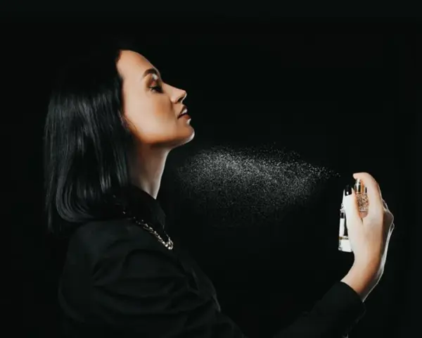 Kobieta rozpyla perfumy na szyję na czarnym tle.