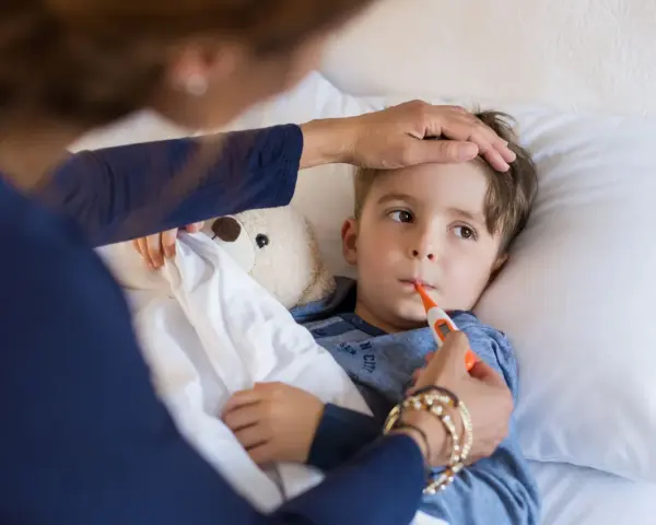 Chłopiec leży w łóżku, mama mierzy mu temperaturę. Znowu choruje, to już drugi raz w tym miesiącu.