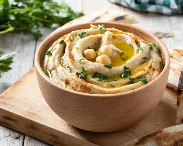 Hummus cremoso en cuenco de madera, decorado con garbanzos, aceite de oliva, perejil y pimentón.