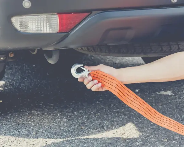 Dłoń mocuje hak liny holowniczej do haka holowniczego auta. To pokazuje, czy można holować auto na linie.