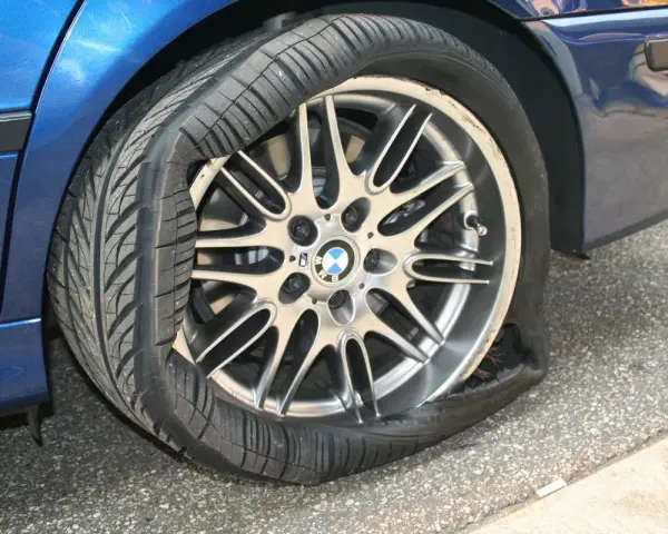 Un pneumatico squarciato sul cerchione di un'auto blu. La gomma è completamente sgonfia e deformata, mostrando il danno.