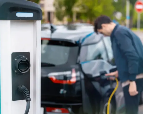 Mój elektryk czeka na ładowanie. Mężczyzna podłącza kabel do samochodu przy stacji ładowania.