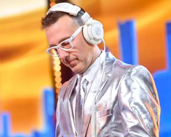 DJ w błyszczącej marynarce i białych okularach, słuchawki na uszach, gotowy do zagrania "Jaka to melodia".