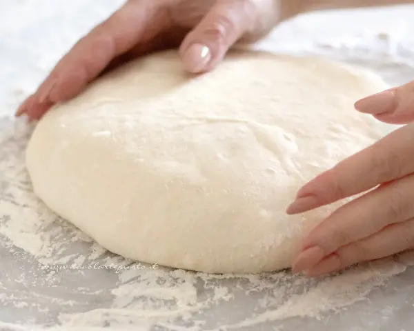 Mani che lavorano un impasto pizza veloce, soffice e pronto per essere steso.