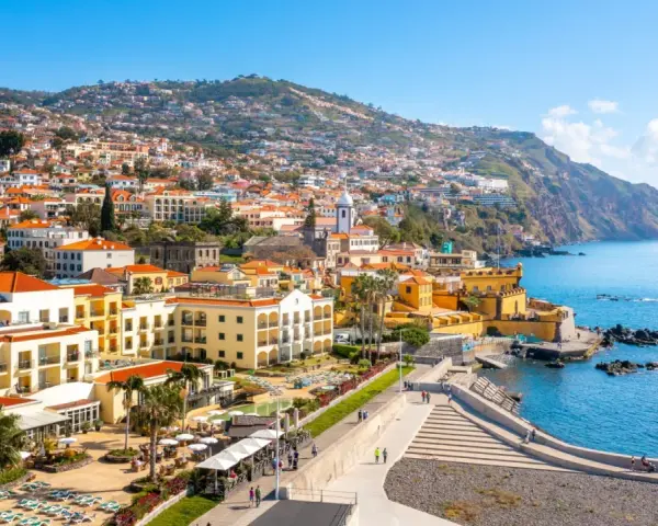 Widok na Funchal, stolicę Madery, z kolorowymi budynkami wznoszącymi się na zboczu góry, otoczonymi błękitnym oceanem.