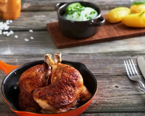 Złociste udka z airfryer w pomarańczowej patelni, obok ziemniaczki i surówka z ogórka. Pyszny obiad gotowy!