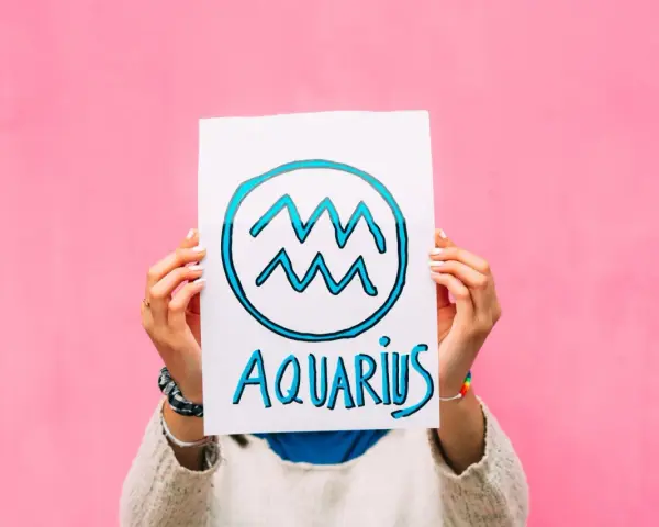 Waga i Wodnik: przyjaźń w kolorach tęczy. Ręce trzymają plakat z symbolem Wodnika i napisem "Aquarius" na różowym tle.