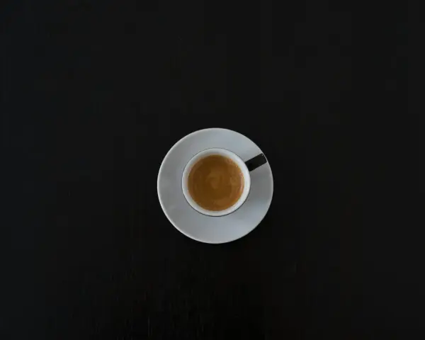Czarna filiżanka espresso na białym spodeczku na ciemnym tle. Może symbolizować początek walki z objawami odstawienia kofeiny.