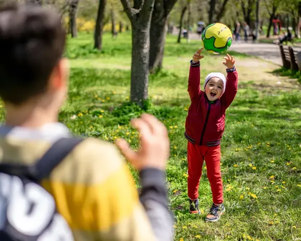 Un enfant joyeux lance un ballon en l'air dans un parc, un autre enfant est devant.
