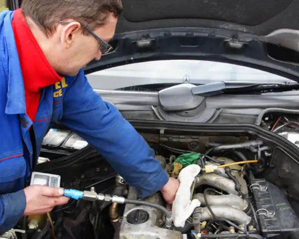 Mechanik w niebieskim kombinezonie sprawdza silnik diesla, używając przyrządu.