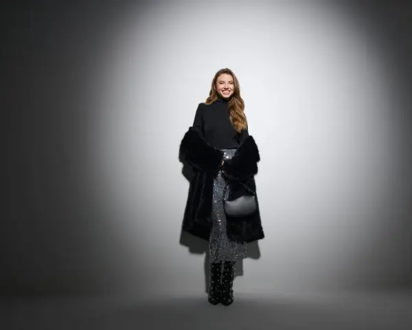 Uśmiechnięta kobieta w błyszczącej spódnicy i futrzanym płaszczu. Czy do filharmonii trzeba ubrać się elegancko? Ta stylizacja sugeruje, że tak!