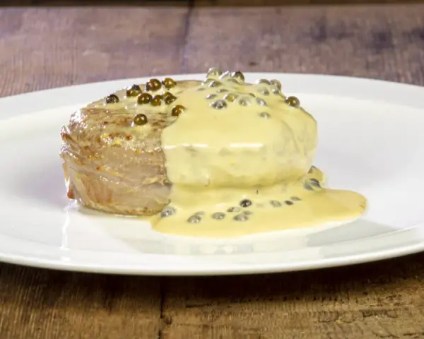 Un succulento filetto al pepe verde, ricoperto da una cremosa salsa, servito su un piatto bianco.