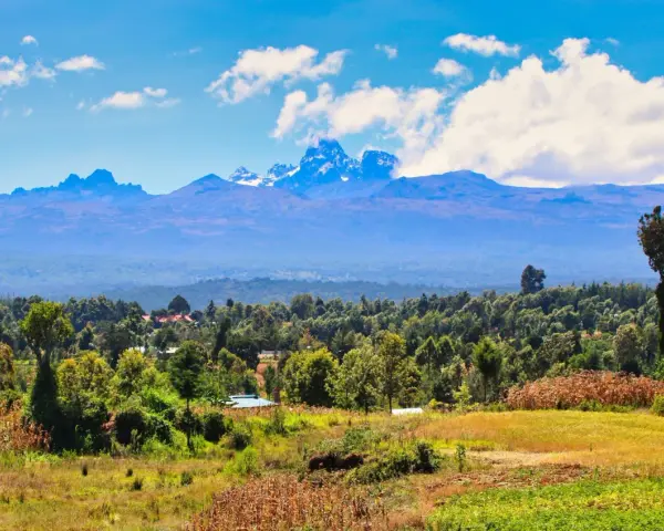Majestatyczne góry Kenii w chmurach, z bujną zielenią i polami u ich podnóża.