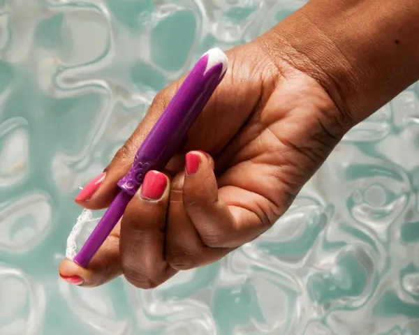 Dłoń z różowym lakierem trzyma fioletowy aplikator tamponu. Pokazano, jak zaaplikować tampon, trzymając go za sznurek.