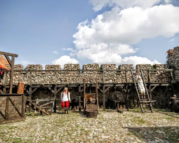 Scena z Muzeum Tortur w Krakowie: gilotyna, postacie w strojach historycznych i kamienne mury.