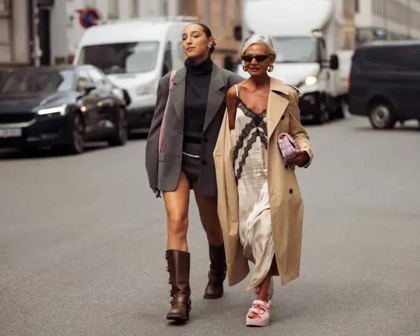 Dos mujeres pasean por la calle. Una lleva un vestido lencero de invierno con un abrigo y la otra un traje gris.
