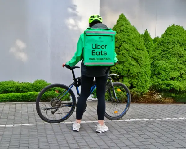 Dostawca Uber Eats w zielonej kurtce i kasku stoi obok roweru.