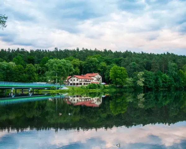 Malowniczy hotel nad jeziorem, z mostem i lasem w tle. Idealne miejsce na wypoczynek i odkrywanie tleń atrakcji.