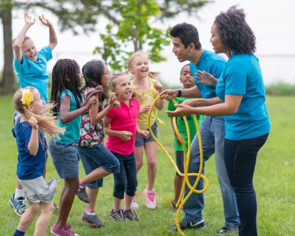 Des enfants et des animateurs jouent à la corde à sauter dans un parc.