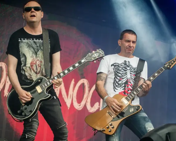 Dwóch gitarzystów na scenie, jeden w czarnej koszulce z sercem, drugi w białej z żebrami. Kocham cię jak Irlandię, grają rocka.