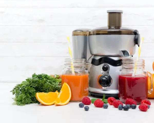 Une centrifugeuse ou extracteur prépare des jus frais avec des fruits et légumes. Ici, des jus d'orange, de carotte et de baies, avec des oranges, des carottes et des baies.