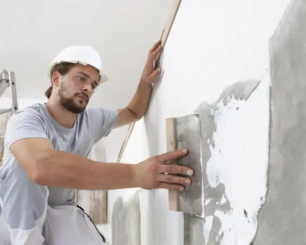 Artisan appliquant un enduit sur béton intérieur, préparant le mur pour une finition parfaite.