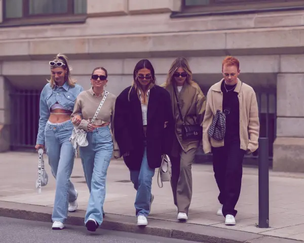 Fünf Freunde spazieren lässig, alle tragen Jeans. Welche Jeans sind in? Weite Schnitte und helle Waschungen dominieren den Look.