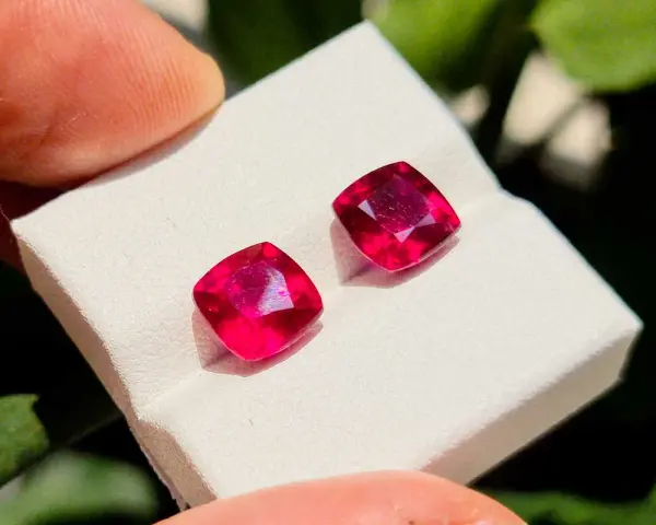 Due gemme rosse intense, la pietra di luglio per eccellenza, brillano su un supporto bianco.