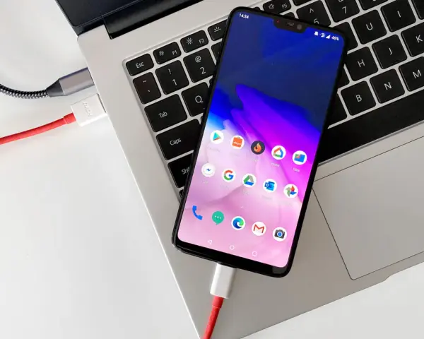 Smartfon podłączony kablem do laptopa, gotowy do przenoszenia zdjęć.