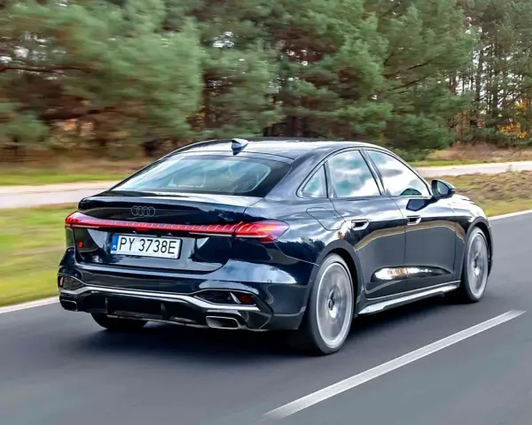 Ciemny Audi A4 B10 pędzi po drodze, otoczony jesiennym lasem.