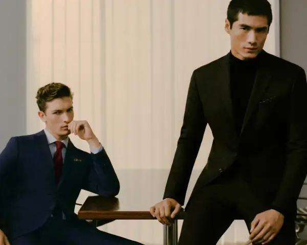 Dos hombres con trajes elegantes, uno azul y otro negro, demuestran el estilo business casual en una oficina moderna.