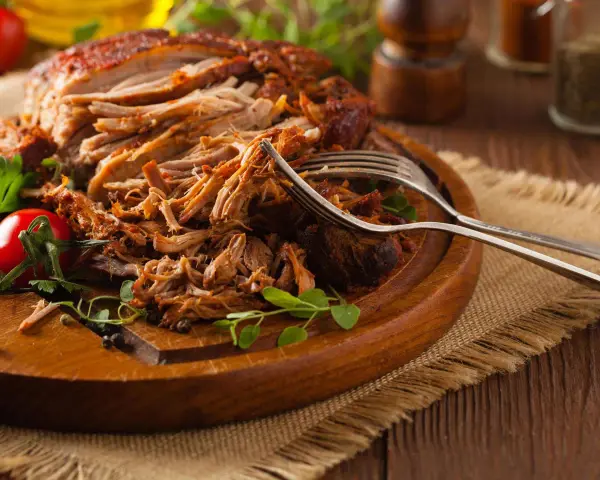 Saftiges Pulled Pork, perfekt zubereitet mit einem aromatischen pulled pork rub, liegt auf einem Holzbrett. Gabeln deuten auf den Genuss hin.