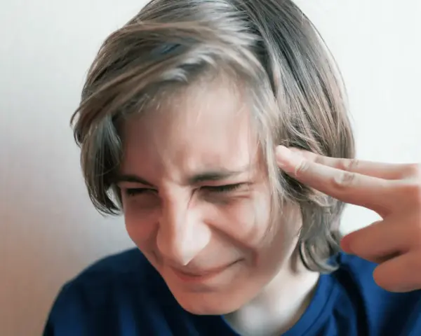 Chłopak z palcami przy skroni, zaciśniętymi oczami, jakby czuł pulsujący nerwiak w głowie.