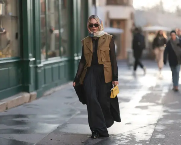 Mujer con chaleco negro corto, falda larga negra y bolso amarillo.