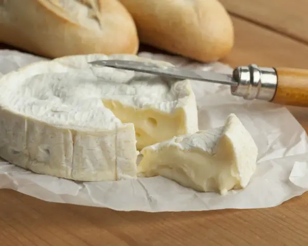 Un trozo cremoso de le camembert, con una rebanada cortada y lista para untar en pan crujiente.