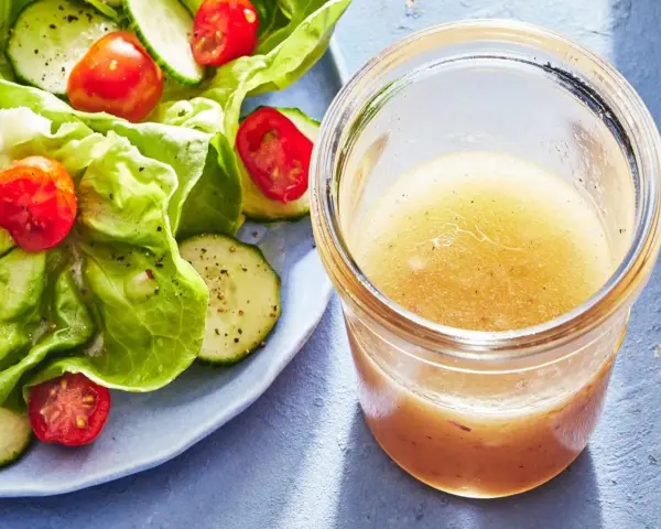 En burk med gyllene dressing till sallad står bredvid en fräsch sallad med sallad, gurka och tomater.