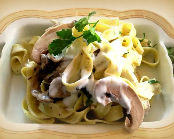 Pyszne tagliatelle z grzybami w kremowym sosie, udekorowane natką pietruszki.