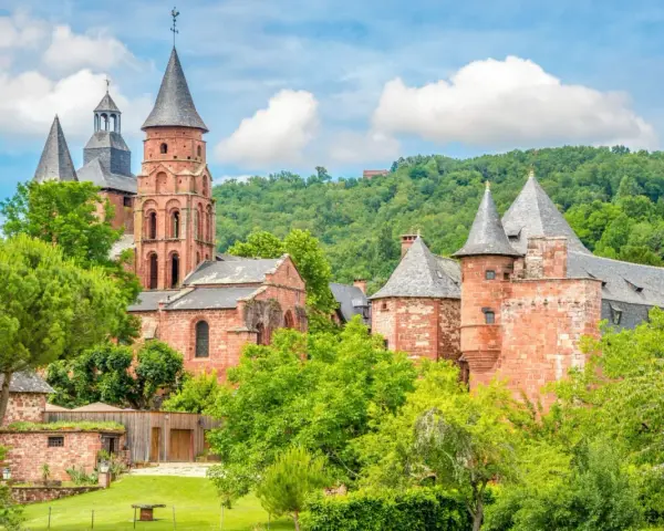 Magnifique ensemble de bâtiments en pierre rouge, dont une église romane et des tours, au milieu d'une végétation luxuriante. Idéal pour découvrir que faire autour de Rocamadour.