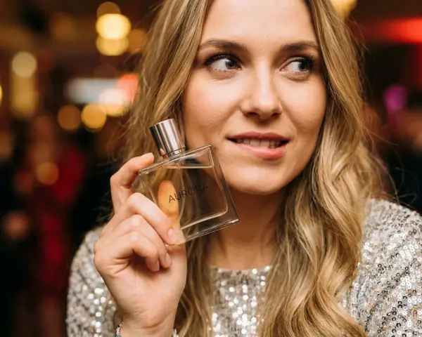 Kobieta z flakonem perfum "Aurora" zastanawia się, czy ma w sobie to coś, co przyciąga mężczyzn.