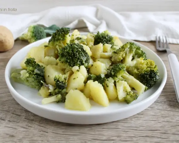 Un plato de brócoli con patatas, sencillo y saludable. Una patata entera y trozos de brócoli reposan cerca.