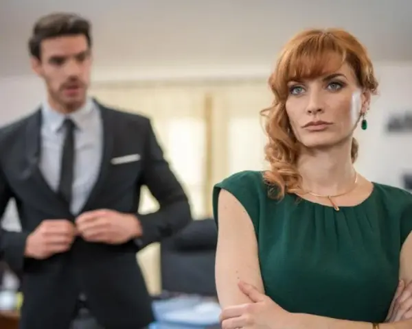 Donna con sguardo preoccupato, mentre un collega in primo piano si sistema la giacca, come se volesse metterla in cattiva luce.