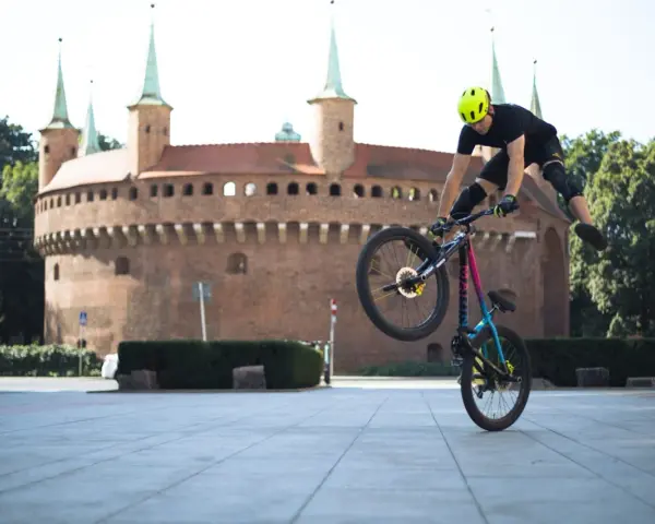 Kraków rowerem: kaskader na rowerze wykonuje akrobację przed Barbakanem.