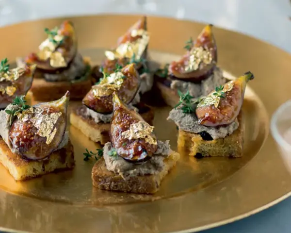 Deliciosos higos con foie sobre tostadas, adornados con pan de oro y tomillo, servidos en una bandeja dorada.