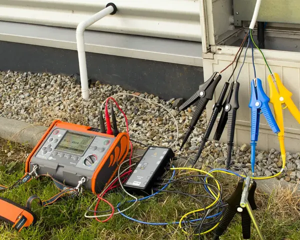 Pomiar rezystancji izolacji instalacji elektrycznej za pomocą miernika. Podłączone przewody z krokodylkami do badanych punktów.