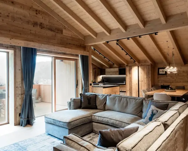 Cozy mountain chalet living room with sectional sofa, wooden beams, and large windows.