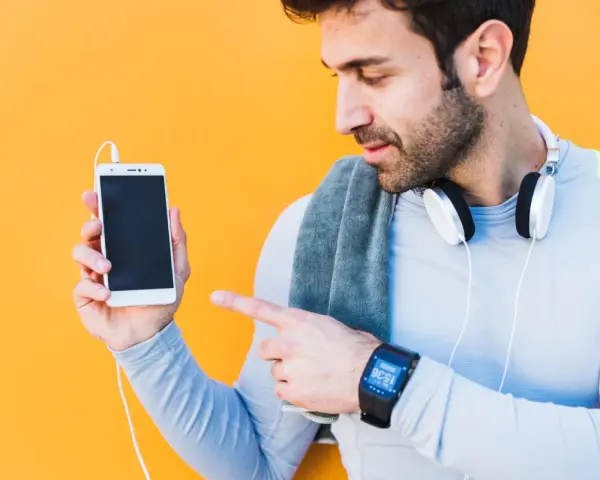 Mężczyzna w sportowym ubraniu pokazuje telefon, jak sparować zegarek z telefonem. Na nadgarstku ma smartwatch.