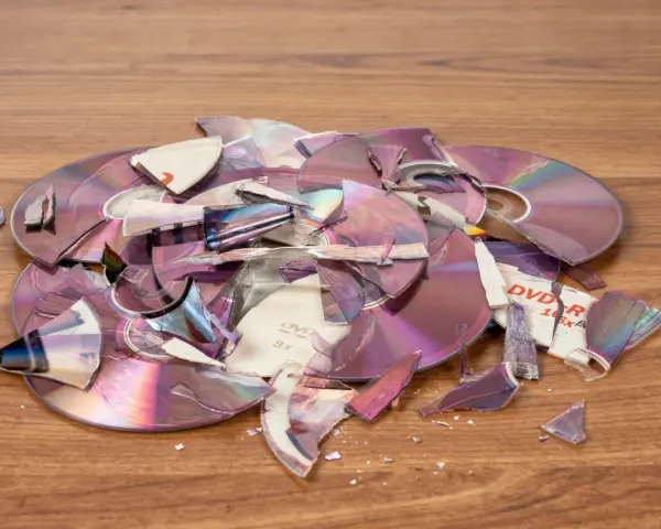 Stos zniszczonych płyt DVD i CD na drewnianym blacie. Czy płyty CD to elektrośmieci? Pytanie o ich utylizację nabiera sensu.