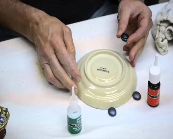 Mani che lavorano per riparare la ceramica con colla e piccoli pezzi.