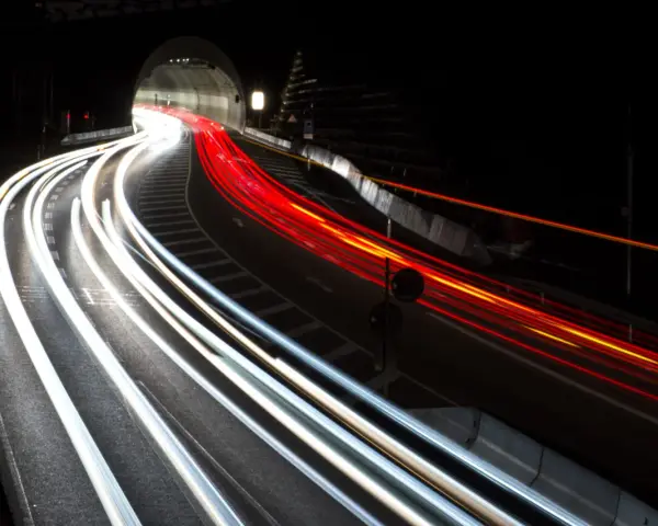 Voiture traversant un tunnel la nuit, capturant les traînées lumineuses des phares et des feux arrière grâce à des photos pose longue.